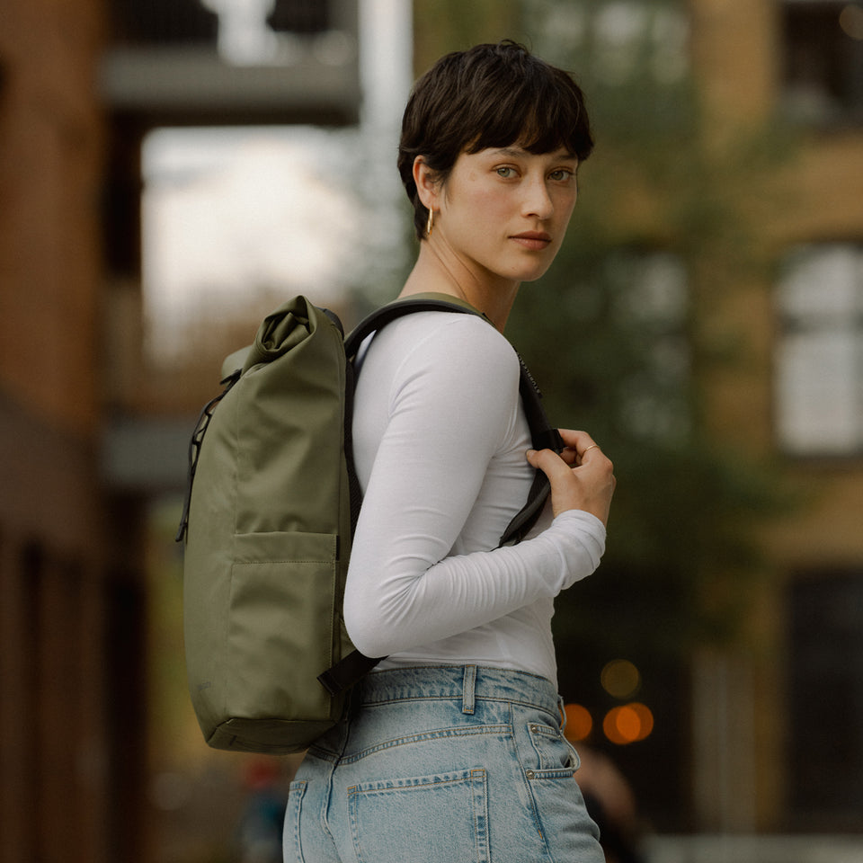 A woman facing side one with a roll top 15l in Urban Green on her back