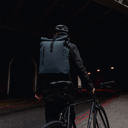 a man standing next to a bike wearing a Roll Top 30L in Tasmin Blue