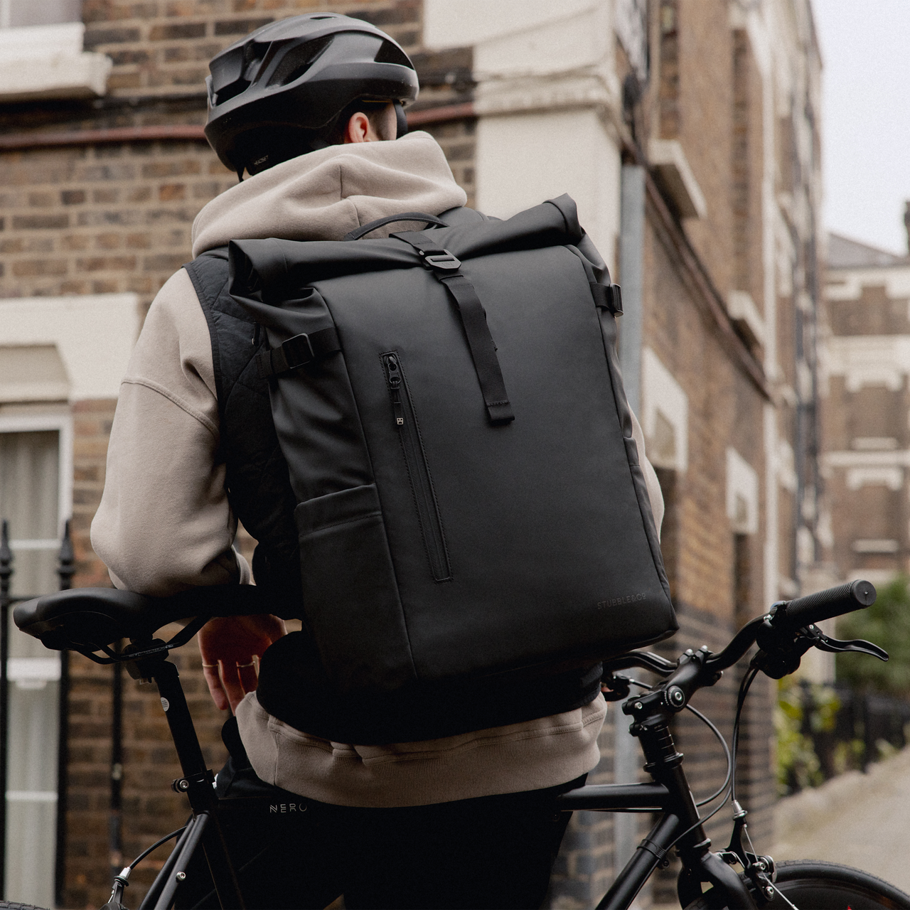 A man with a bike wearing an All Black Roll Top 30L on his back