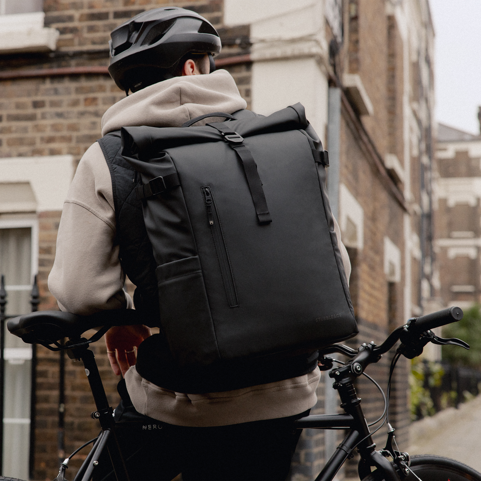 A man with a bike wearing an All Black Roll Top 30L on his back