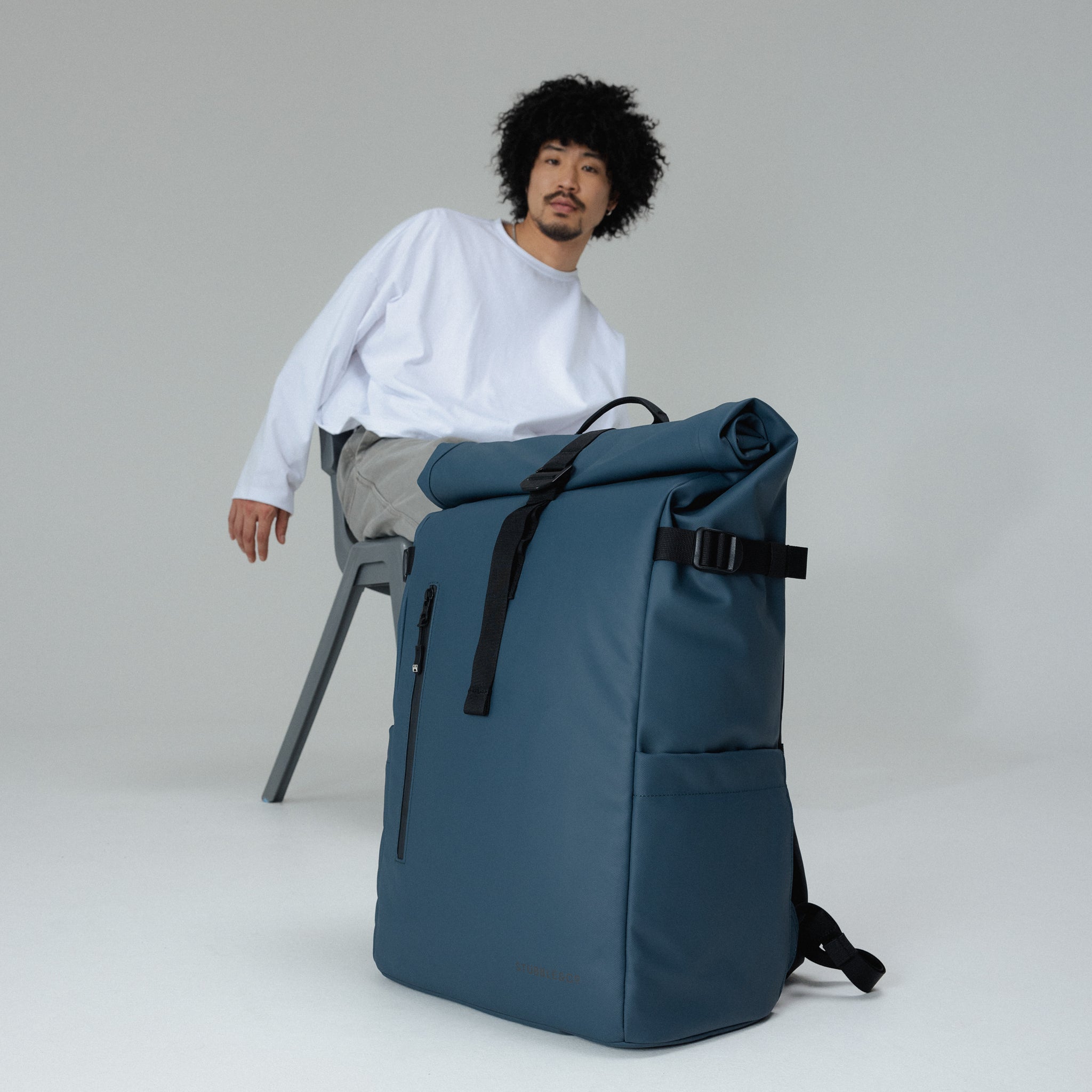 A man sitting on a chair with a Tasmin Blue Roll Top 30L in front of him