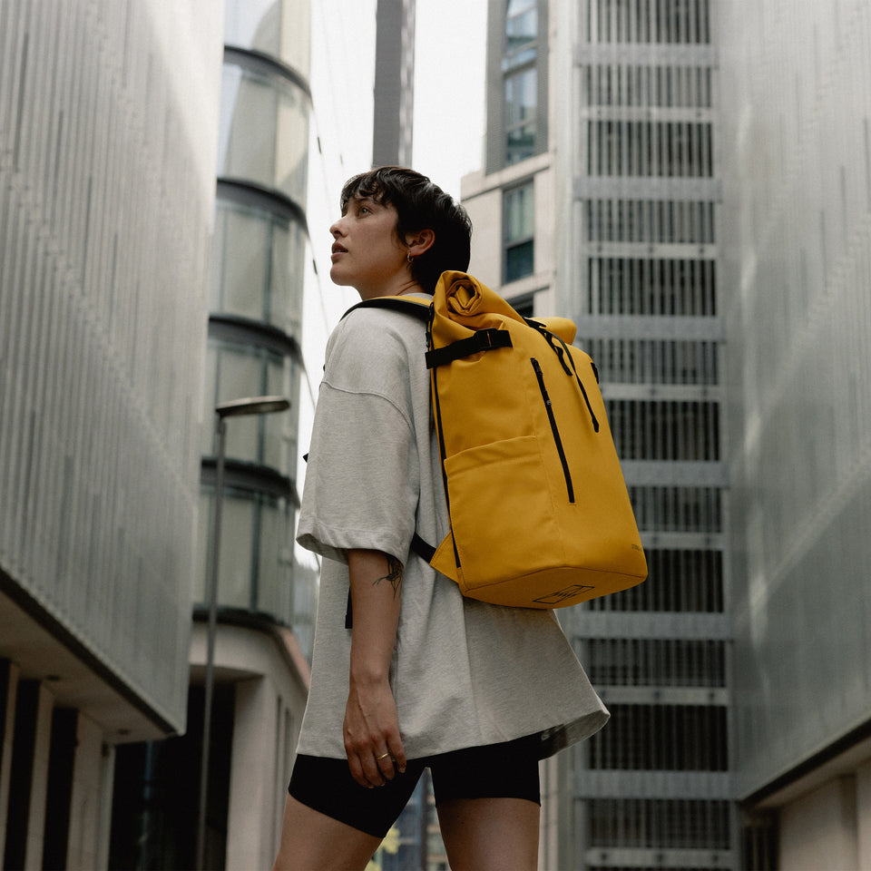 A woman walking wearing a Roll Top 30L in Yellow on her back