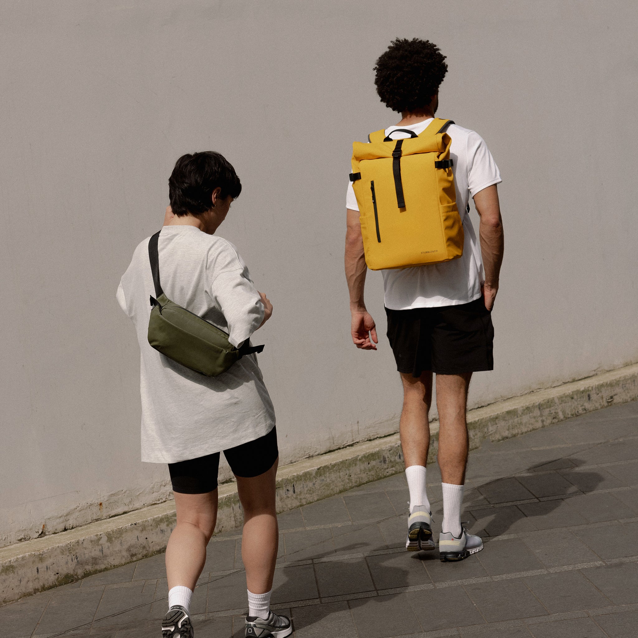 A man walking with a Yellow Roll Top 30L on his woman whilst the woman is wearing a greens crossbody