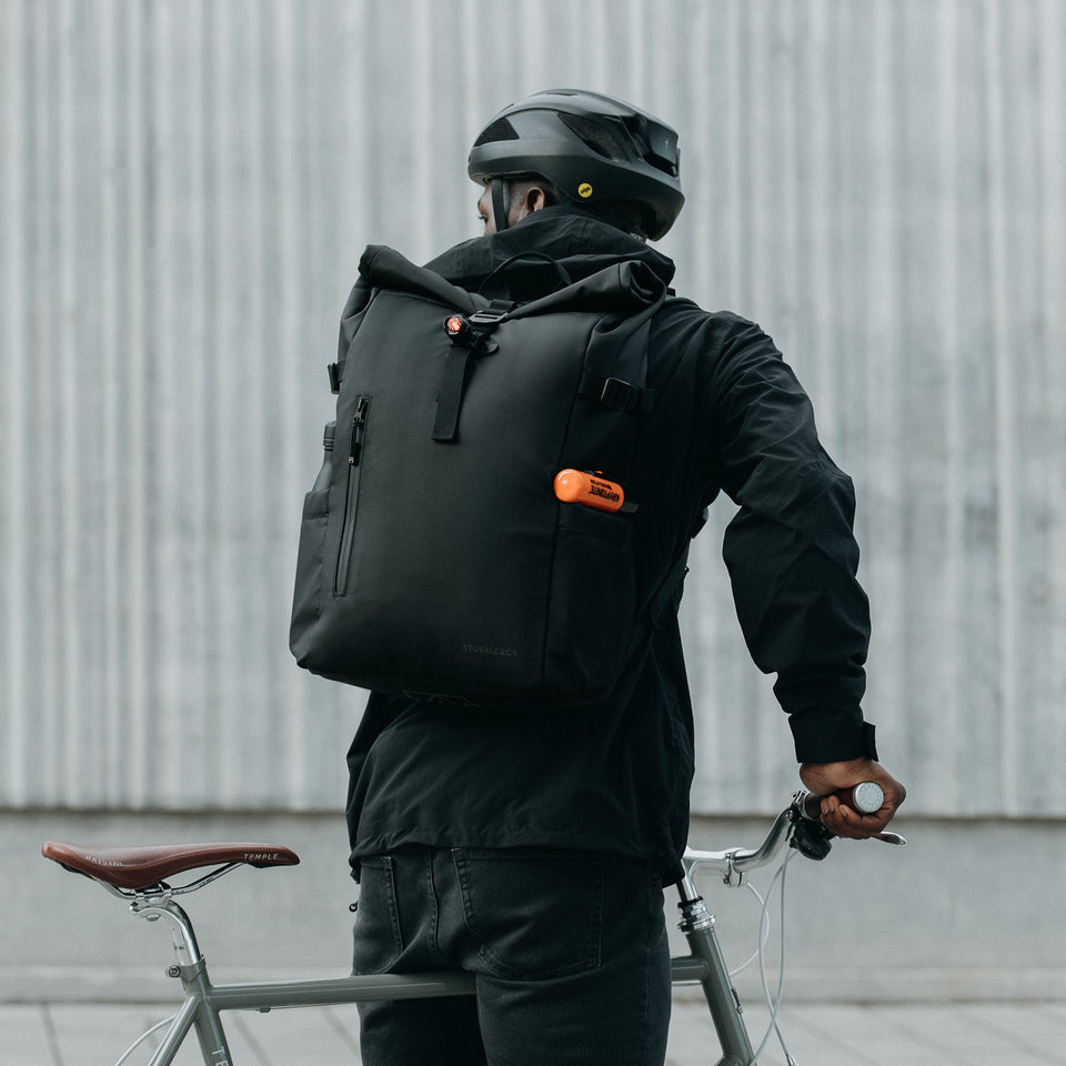 Back view of a man wearing The Roll Top in All Black and a bike helmet, about to cycle off.