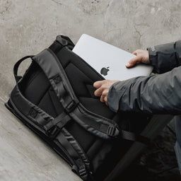 Man putting laptop in Roll Top backpack in All Black