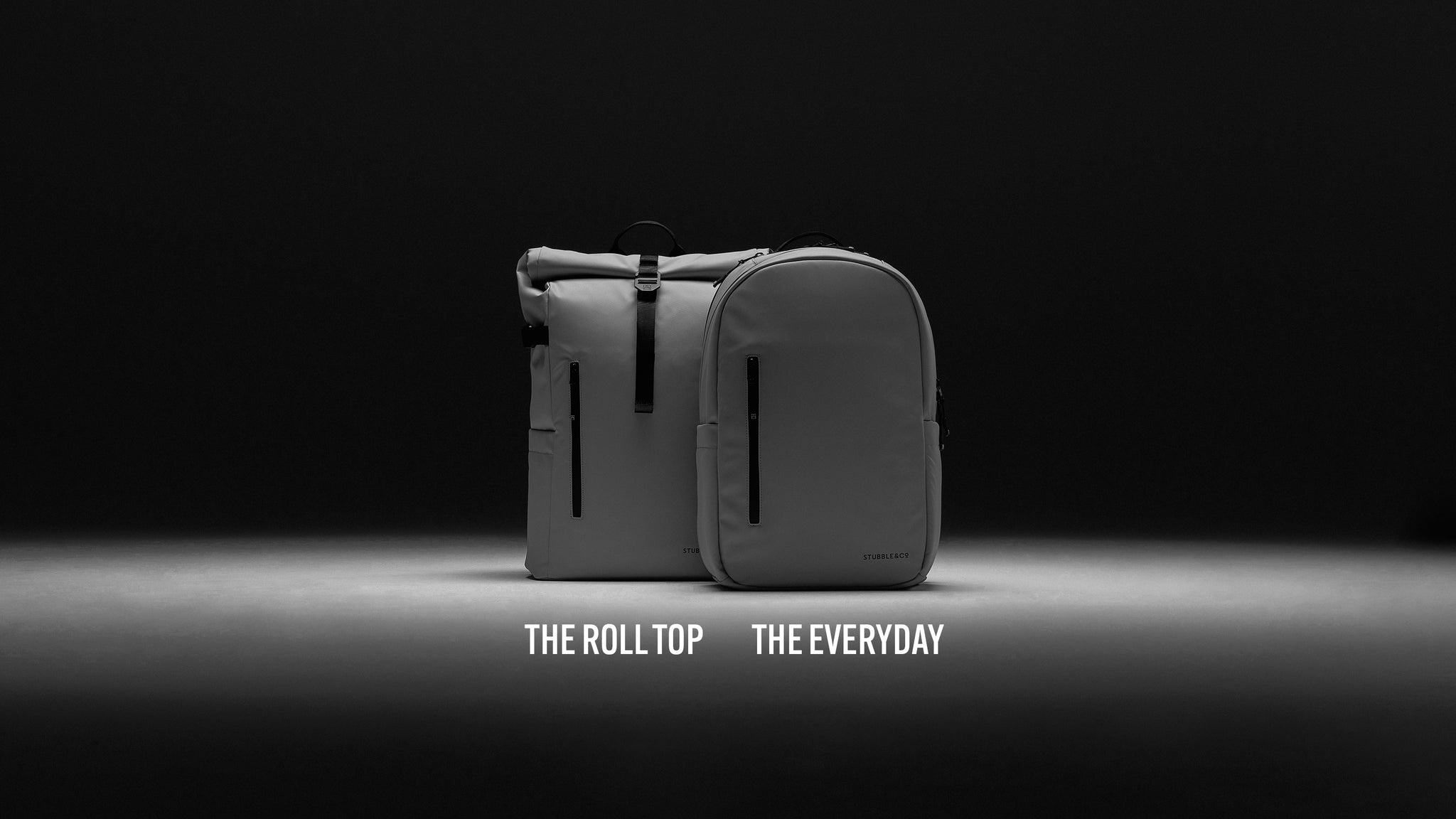 A studio shot of the roll top and everyday back in concrete standing side by side with a black background