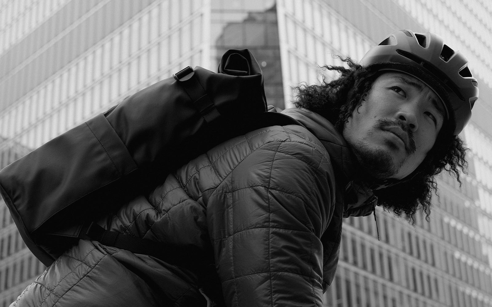 a man with a cycling helmet on and a roll top 20l on his back in a black and white shot