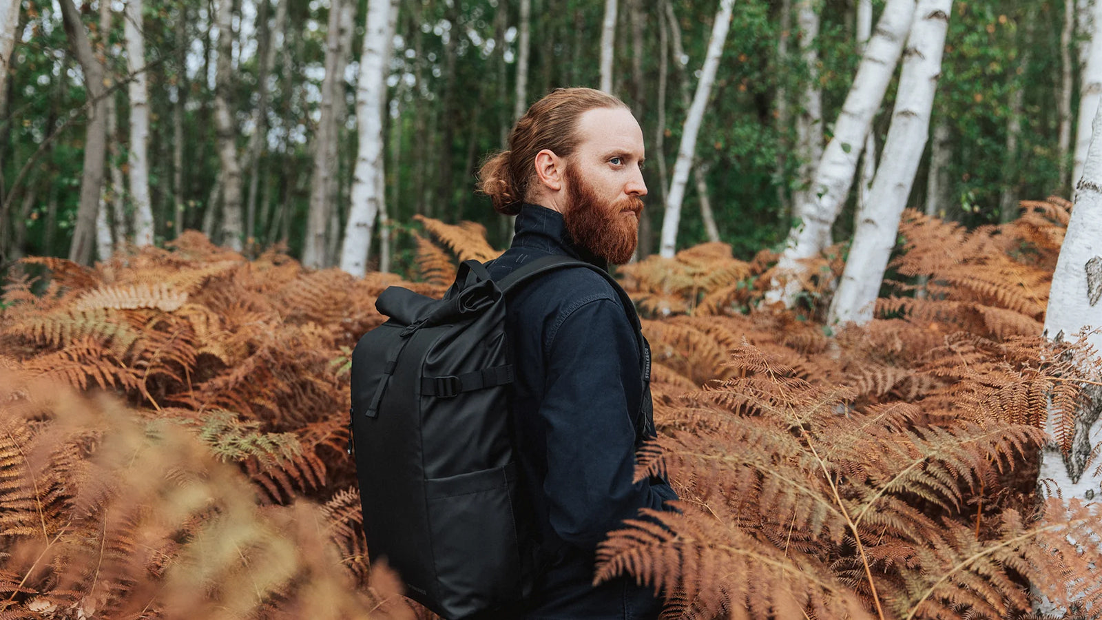 A man standing in a forest with a Roll Top in black on his back