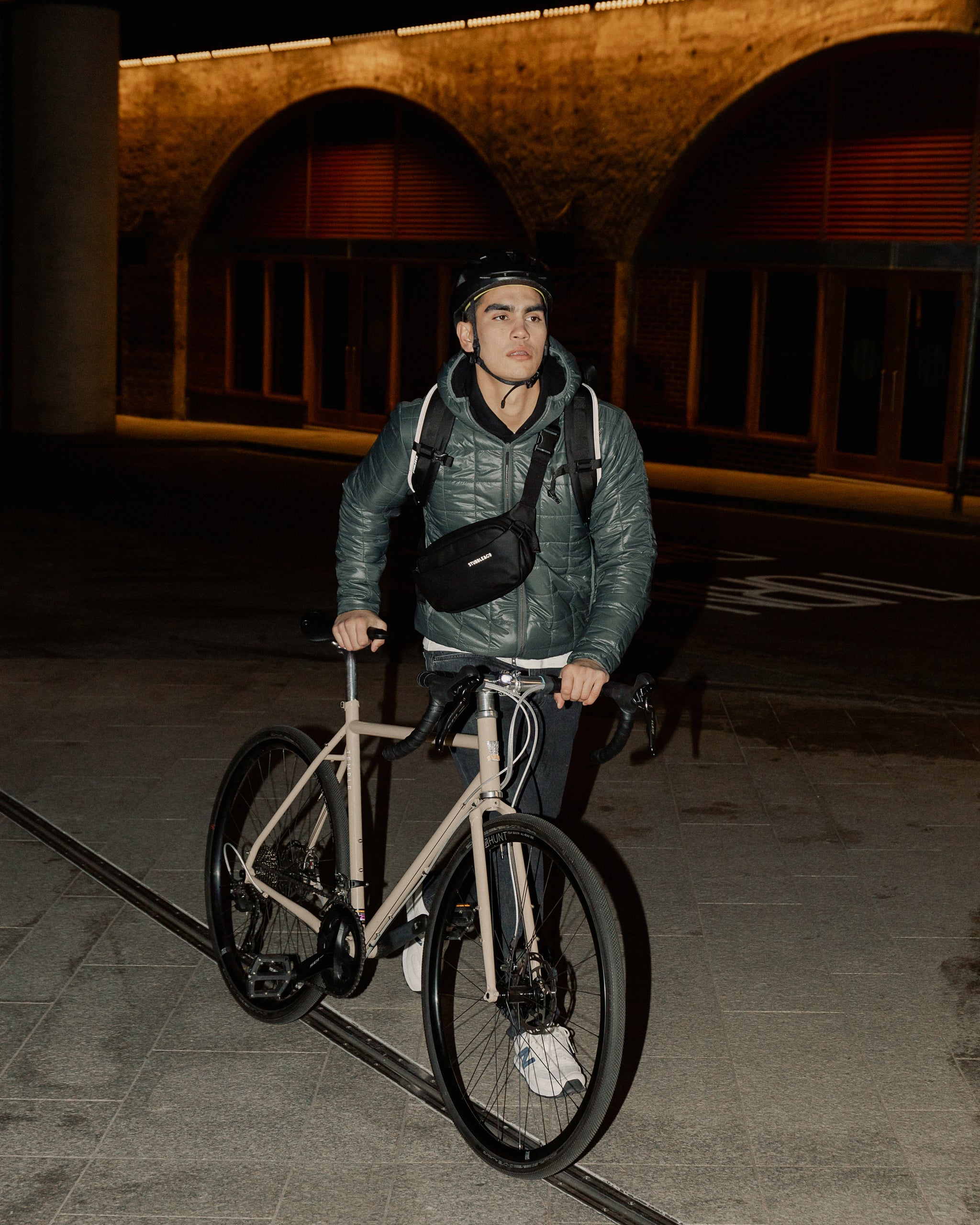 A man pushing his bike whilst wearing a black crossbody and roll top 20l