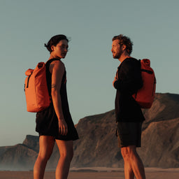 Man and women facing each other on a beach, both wearing The Roll Top in Ember Orange