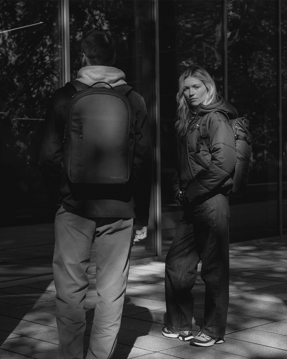 A man wearing an everyday backpack and woman wearing a roll top 20l in black and white