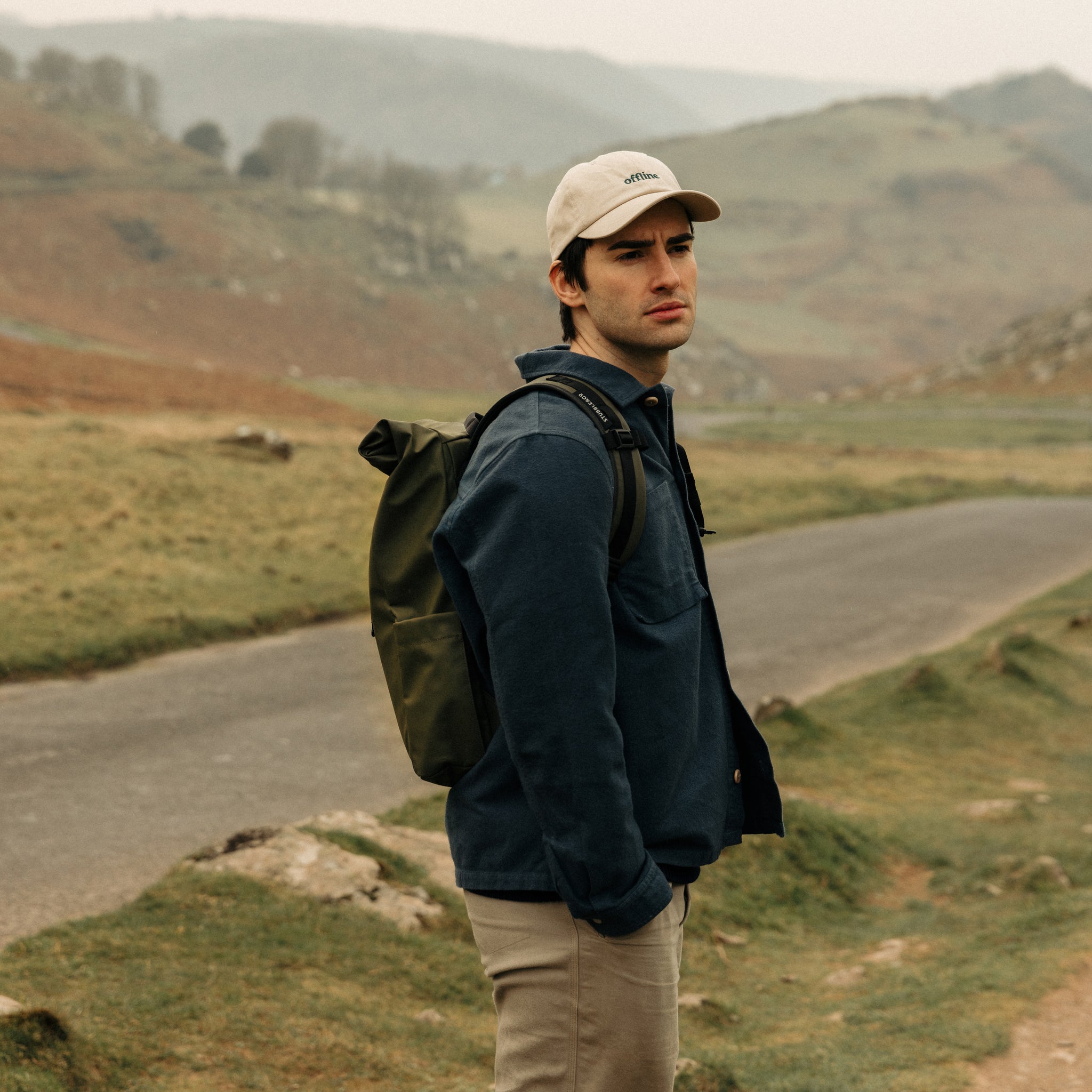 A man standing in a field wearing an Urban Green Roll Top