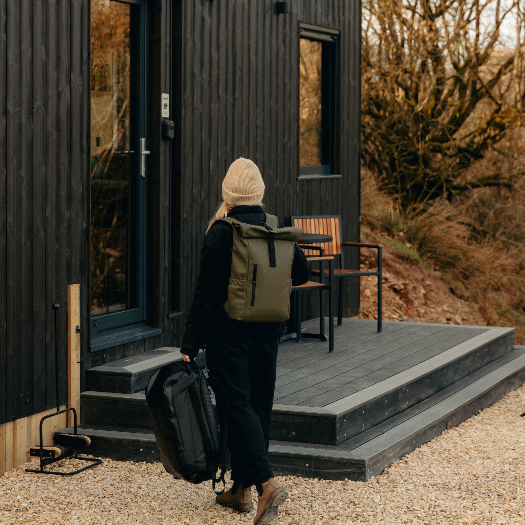 A woman wearing a roll top and carrying a kit bag walking up to an unplugged cabin
