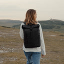 A women in a white long sleeve top and blue jeans walking away from the camera wearing The Roll Top Mini in All Black.