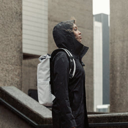 A woman standing in the rain wearing Roll Top Mini backpack in Arctic White
