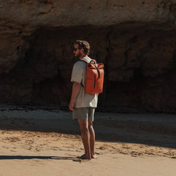 A man standing with a Roll Top Mini backpack in Ember Orange on his back