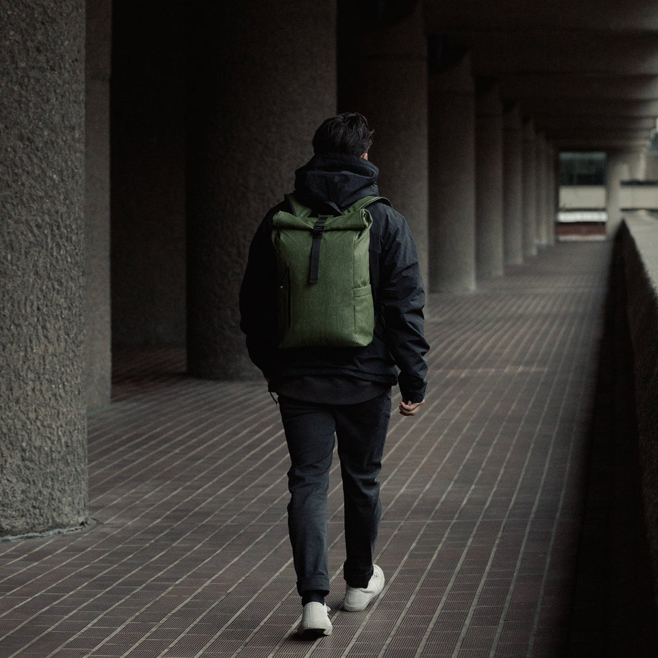 A man walking away from the camera wearing Roll Top Mini backpack in  Urban Green