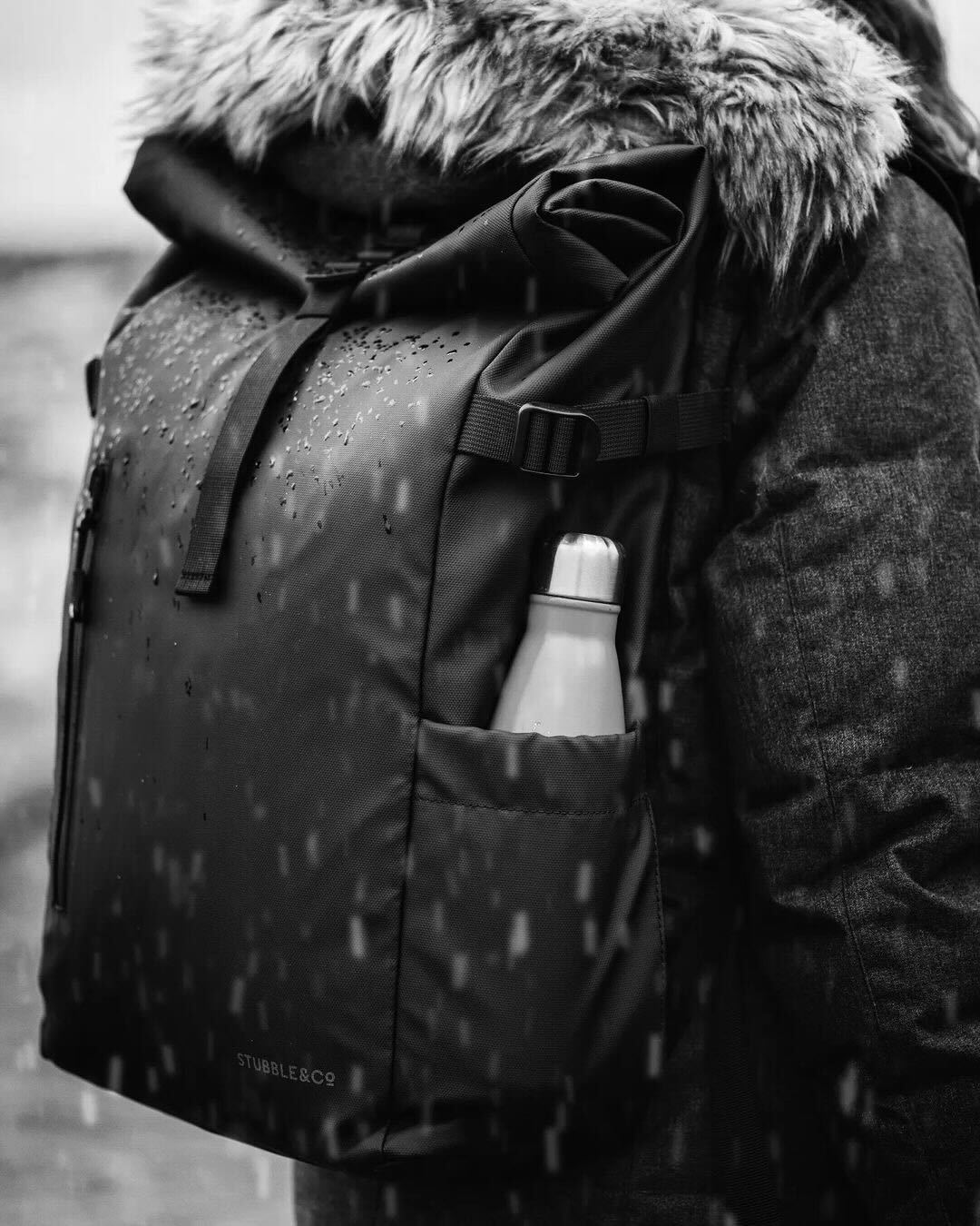 Close up of a person wearing a Black Roll Top backpack in the rain