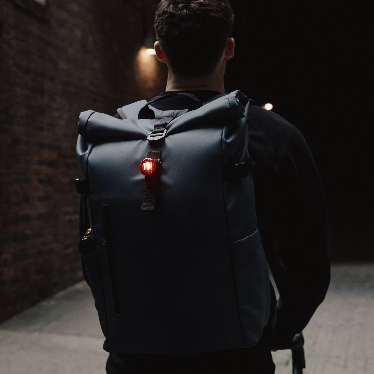 Back view of a man wearing The Roll Top in Tasmin Blue with a bike light on the bag.