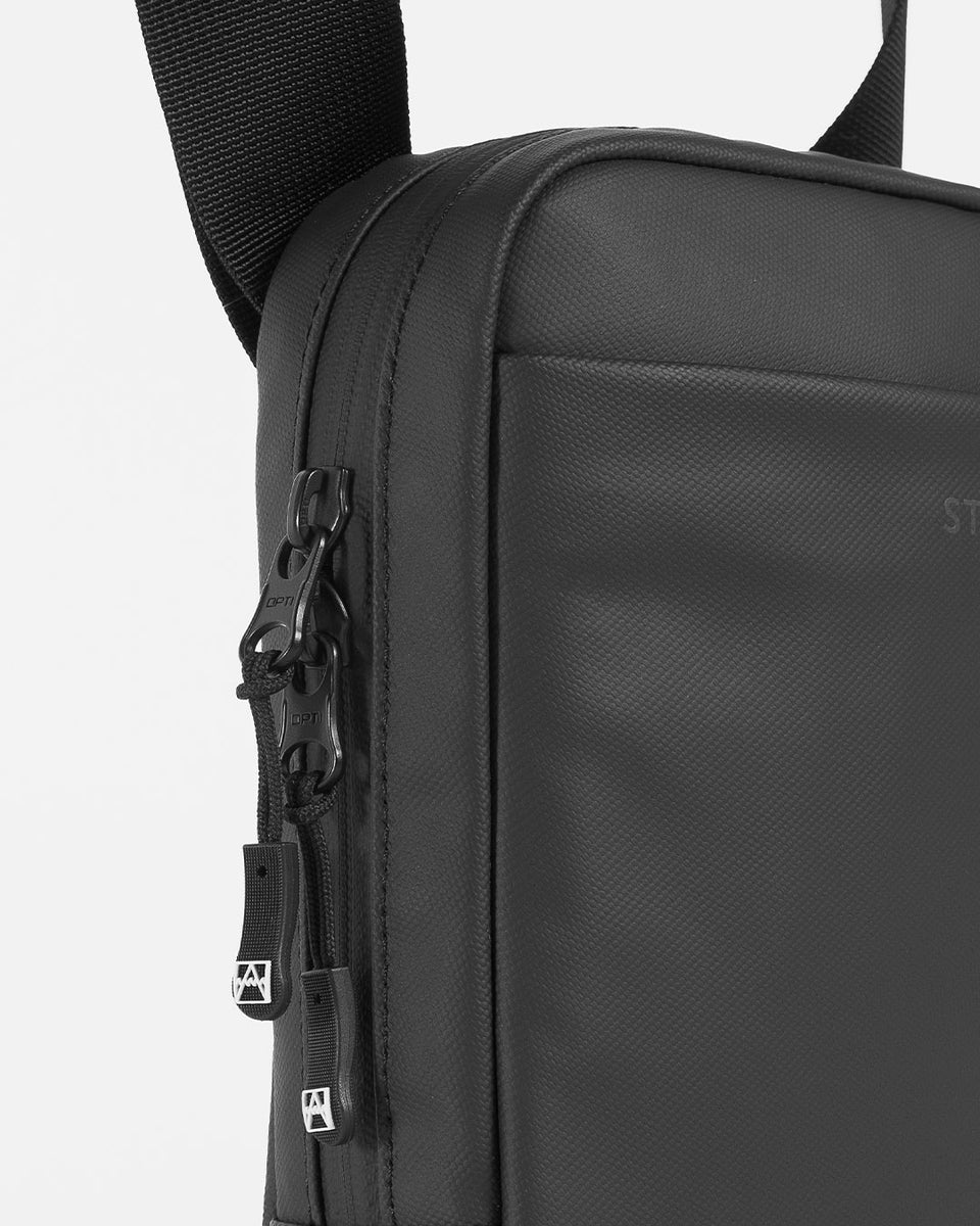 A studio shot of an all black shoulder bag showing the duals zips for two way opening