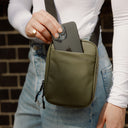 a close up shot of a woman placing her phone in the front slip pocket on an Urban Green shoulder bag