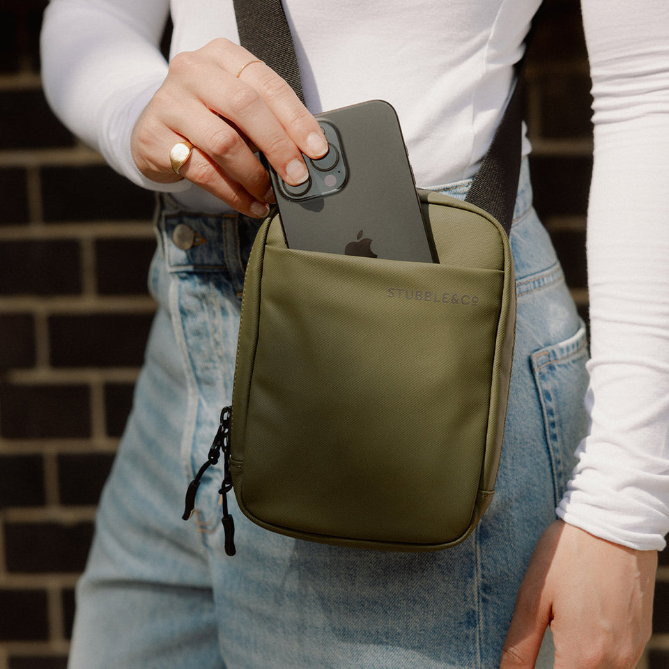 a close up shot of a woman placing her phone in the front slip pocket on an Urban Green shoulder bag