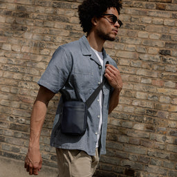 A man walking down the street wearing a Midnight Blue shoulder bag across his body