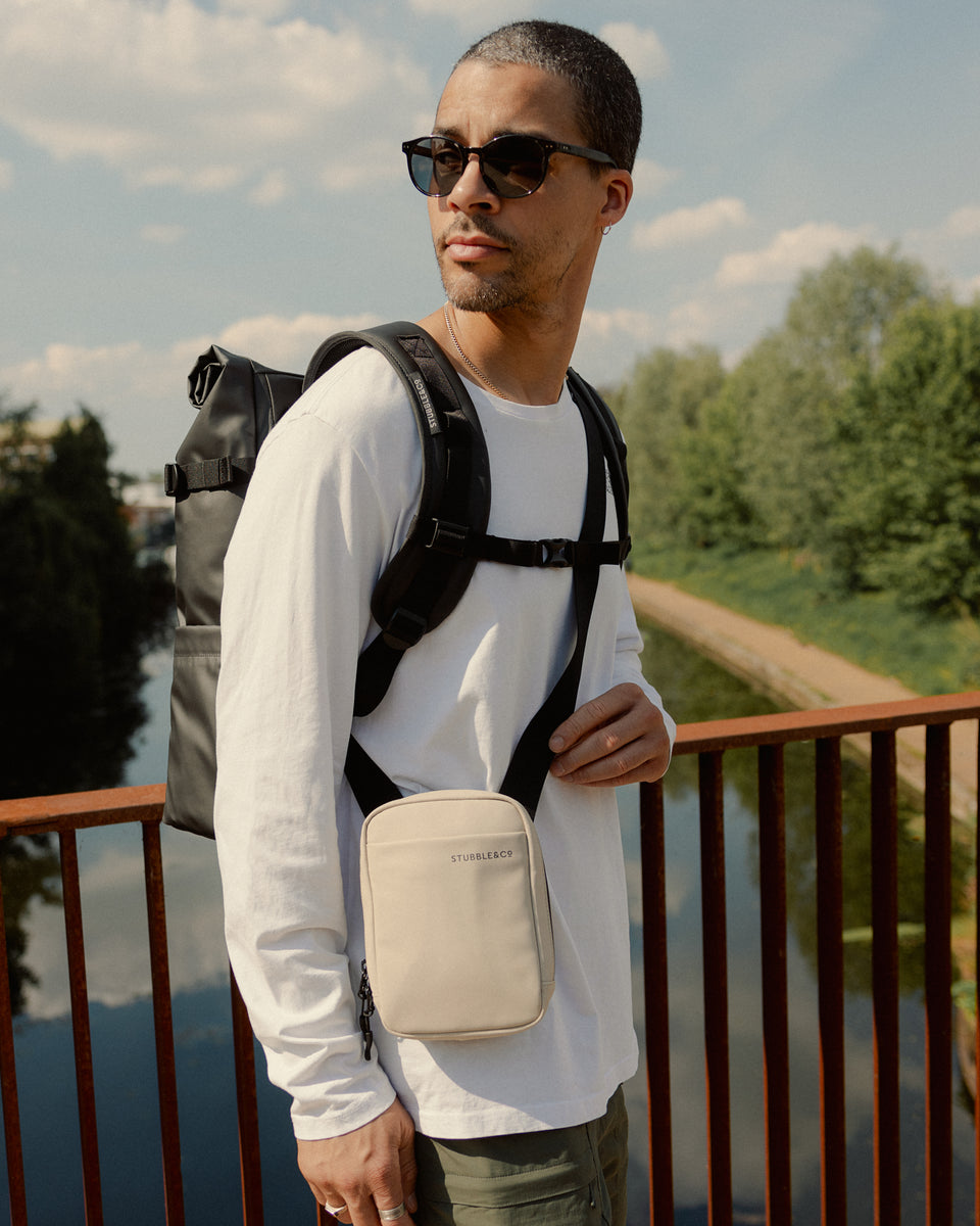 A man on a bridge wearing a roll top and a sand shoulder bag