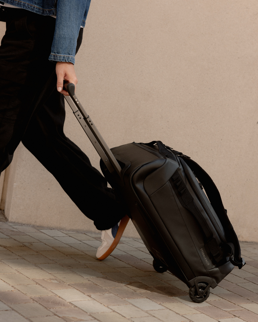 Small suitcase being pulled along a street, the All Black Wheeled Duffel 40L.