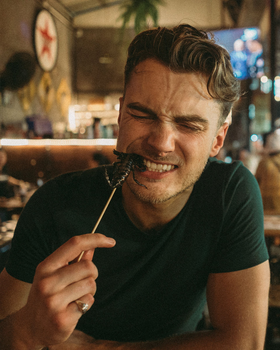 A man from Topjaw, a youtuber, eating a scorpion off a stick in Bangkok