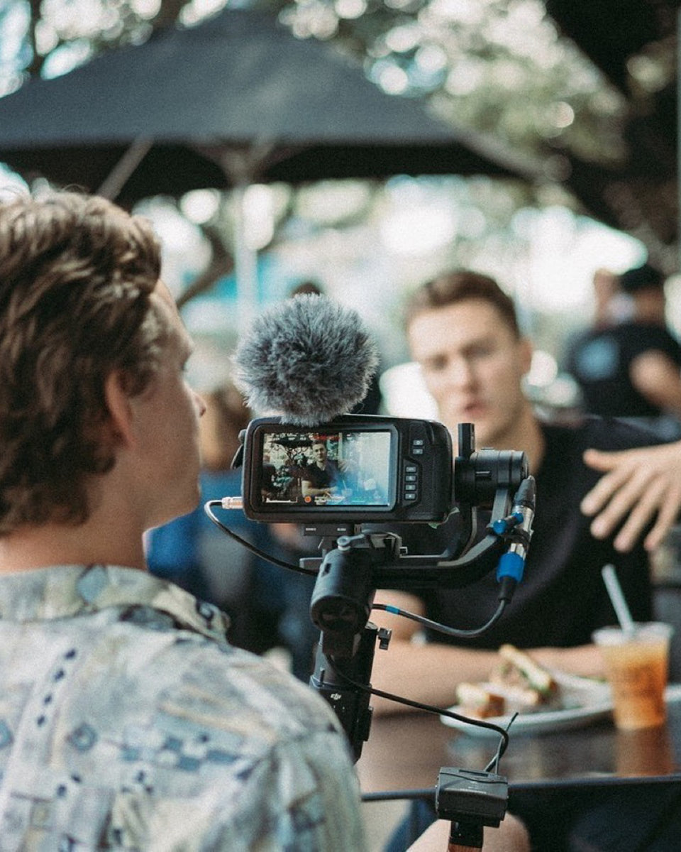 A an holding a recording camera  whilst recording another man