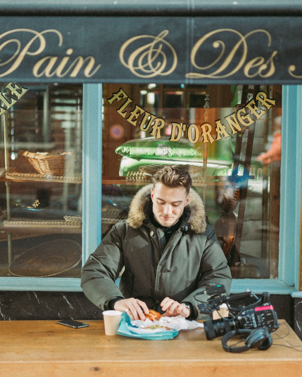 A man from TopJaw, the youtubers, sitting outside a cafe eating his pastry