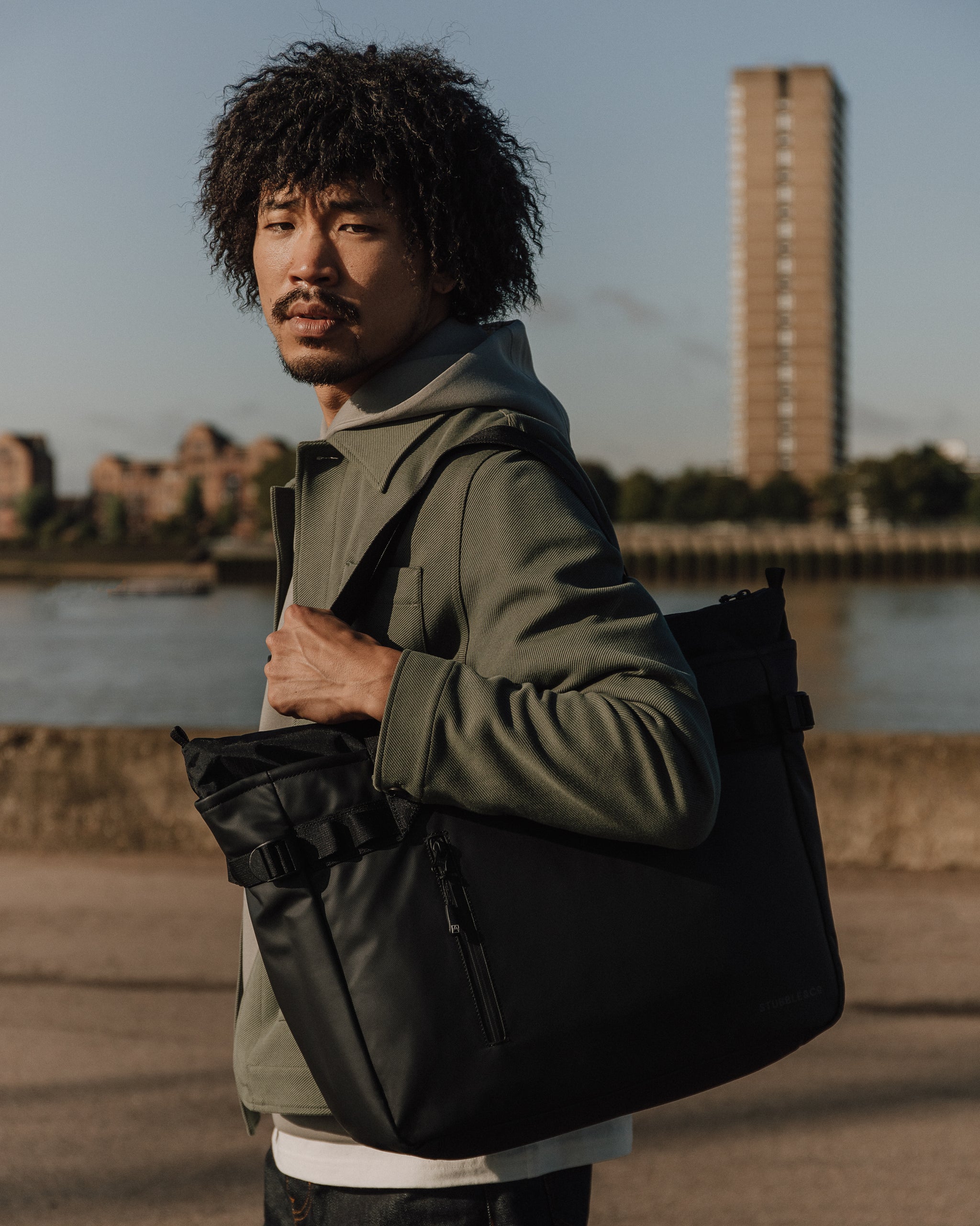 a man wearing a black tote bag on his shoudler in front of a river