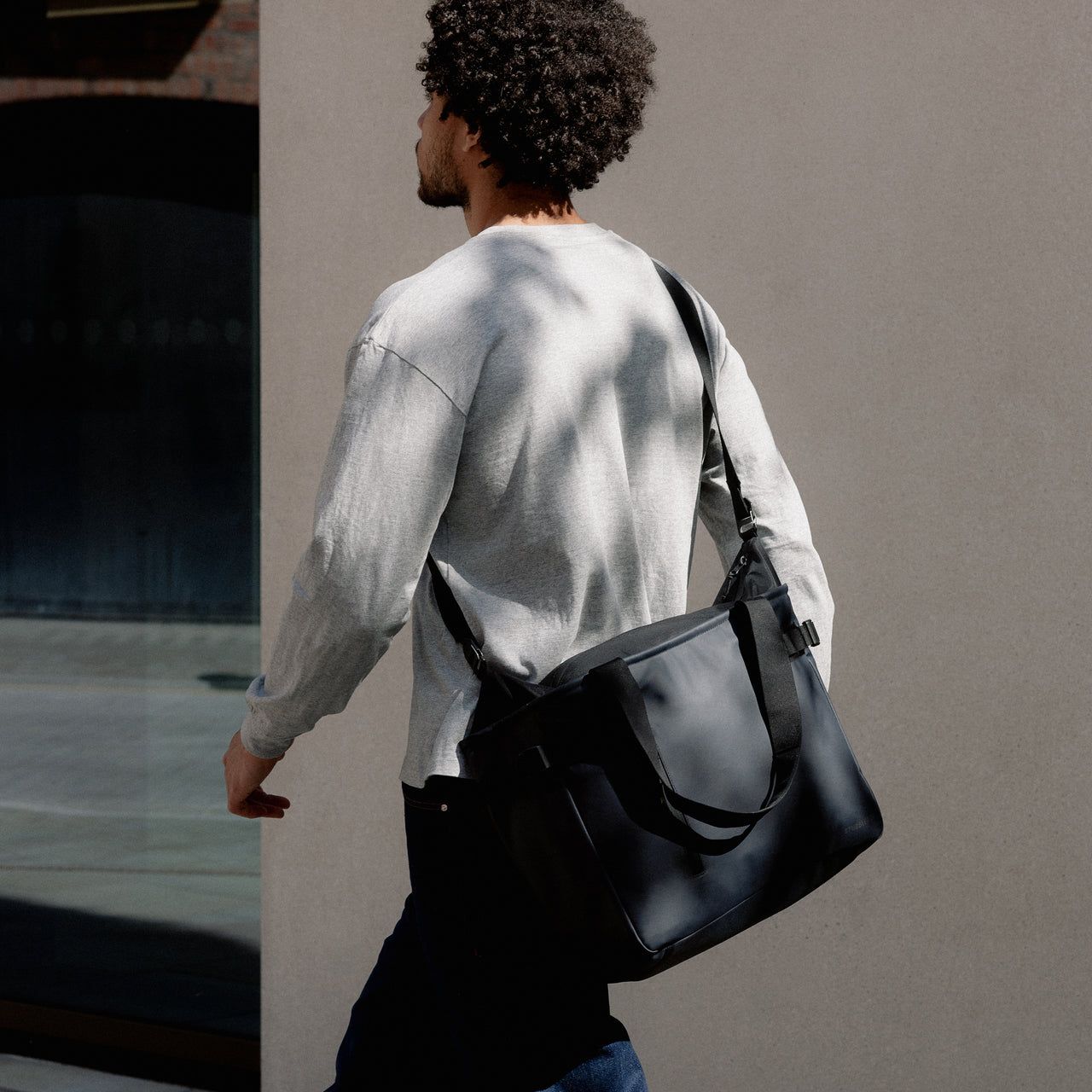 A man walking wearing a Midnight Blue Laptop Tote 20L across his body