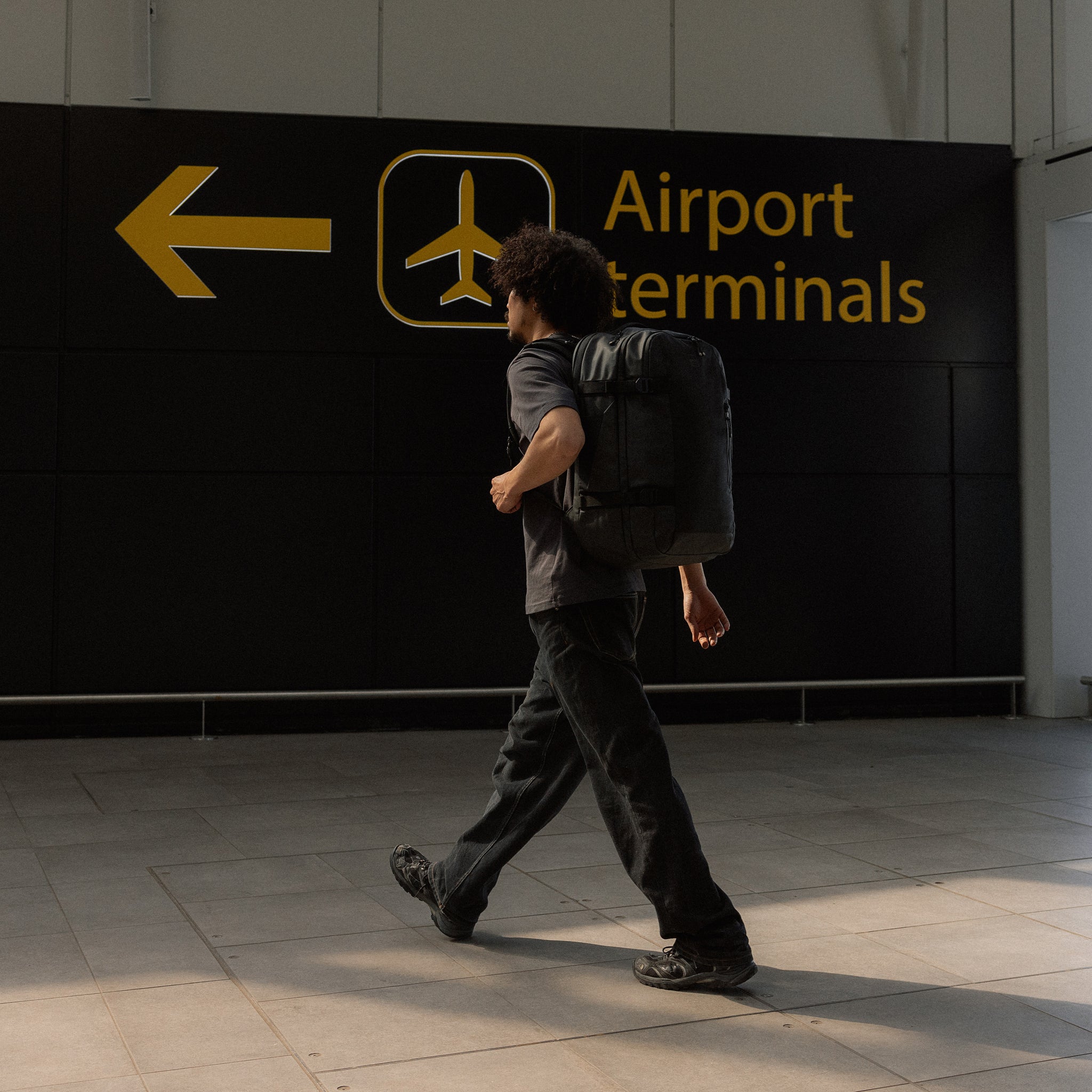 A man walking into an airport terminal wearing an All Black Travel Backpack 40L on his back