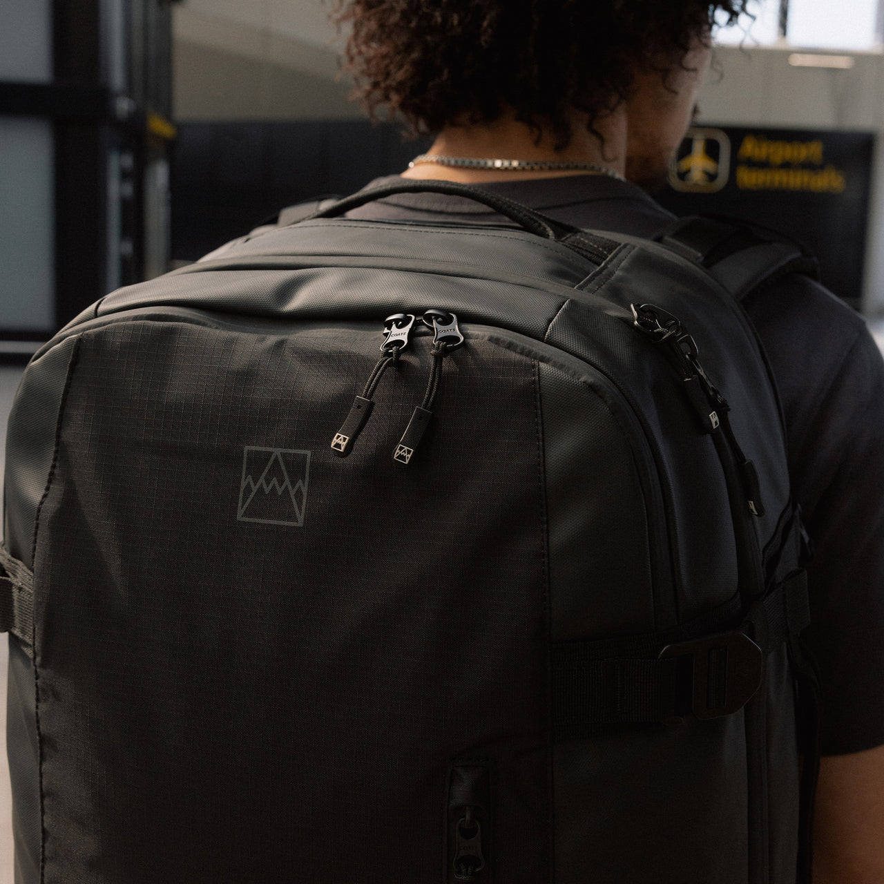 A close up of a Travel Backpack 40L in All Black on a man's back