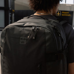 A close up of a Travel Backpack 40L in All Black on a man's back