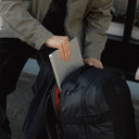 A man putting away his laptop into the laptop compartment in a Travel Backpack 40L in All Black