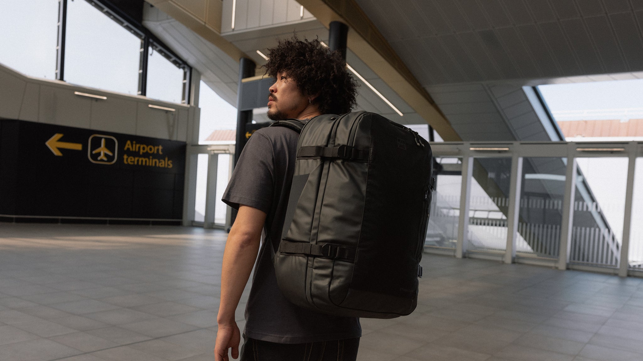 A man standing outside an airport terminal with a travel backpack 40L on his back