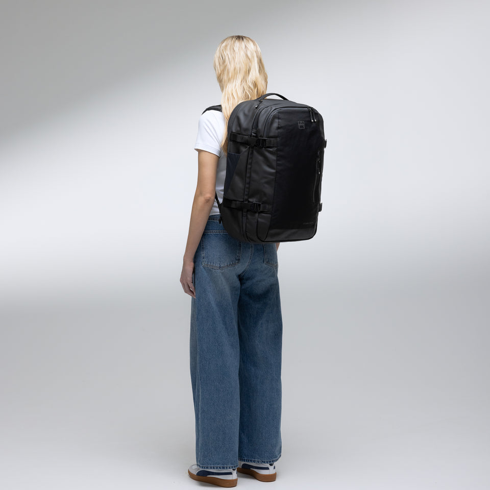 A woman standing in a studio with a black travel backpack 40l on her back