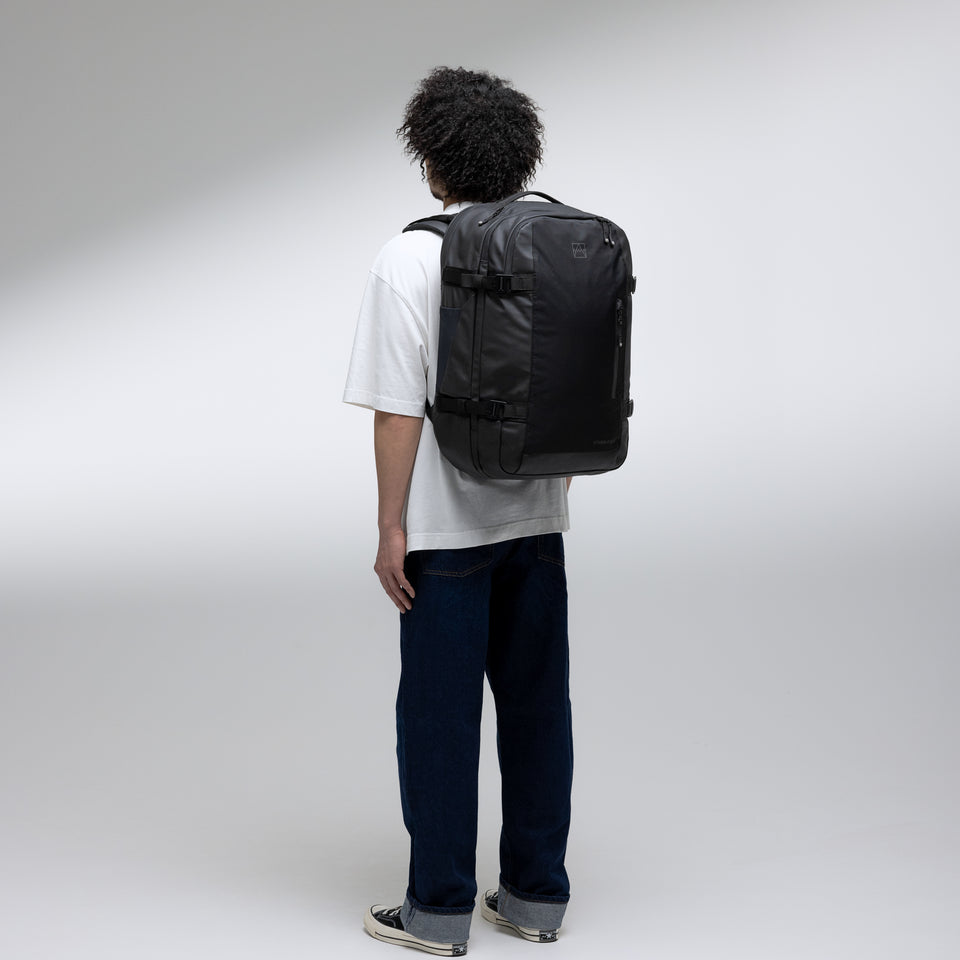 A man standing in a studio with a black travel backpack 40l on his back