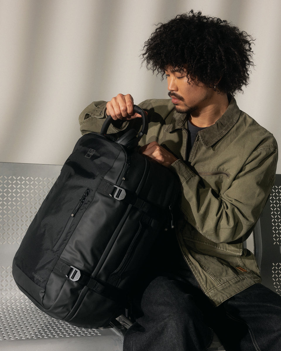 A man sitting on an airport bench putting his headphones into a travel backpack 40l