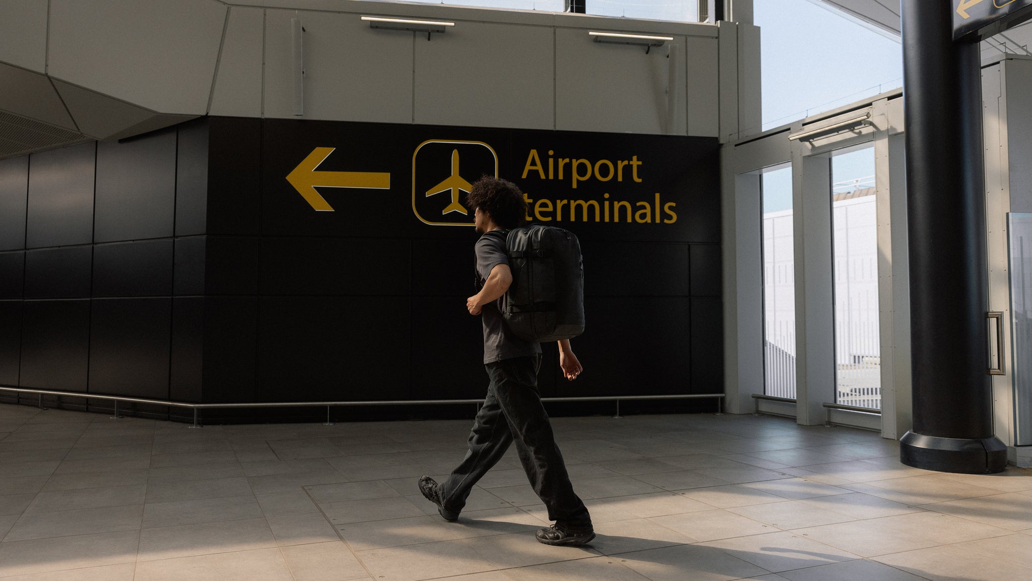 A man walking into an airport terminal with a Travel Backpack 40L on his back