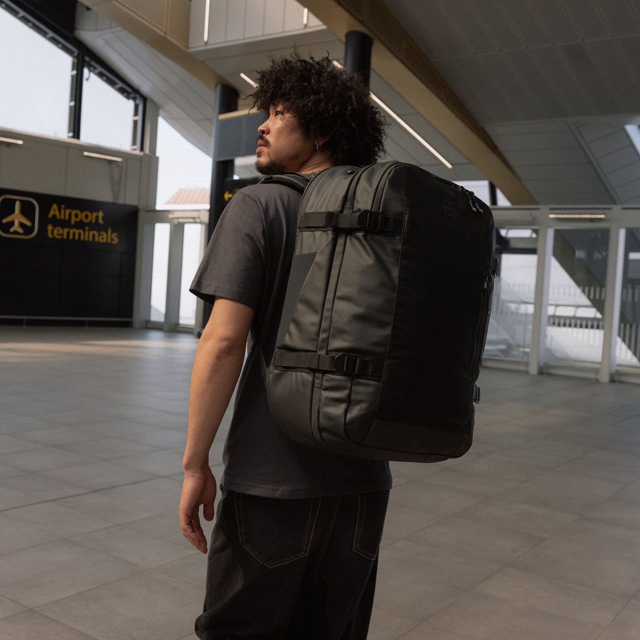 A man standing in an airport terminal wearing a Travel Backpack 40L on his back in All Black