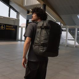 A man standing in an airport terminal wearing a Travel Backpack 40L on his back in All Black