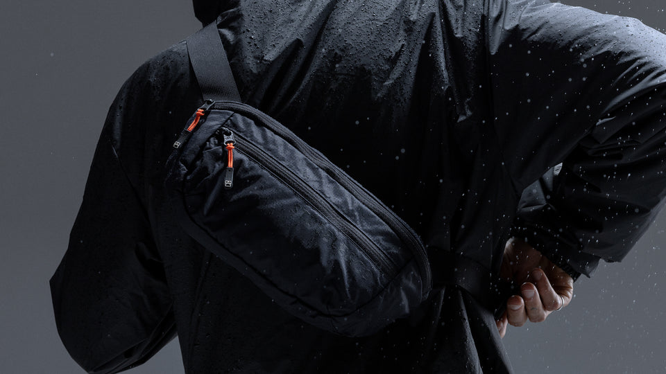 A man wearing a packable sling on his back in a studio with water spraying down