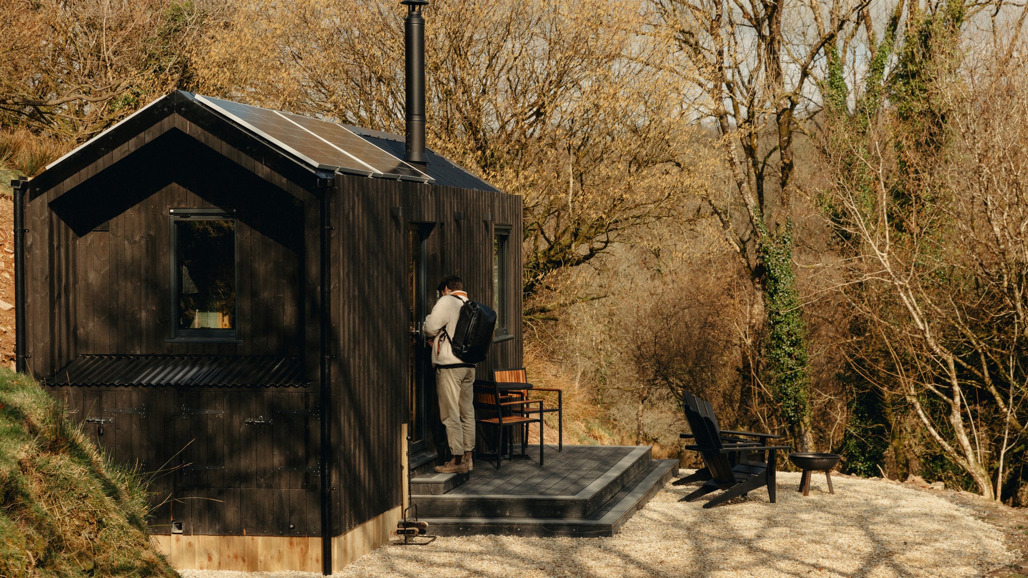 A man at a unplugged cabin wearing a Kit Bag 30l on his back