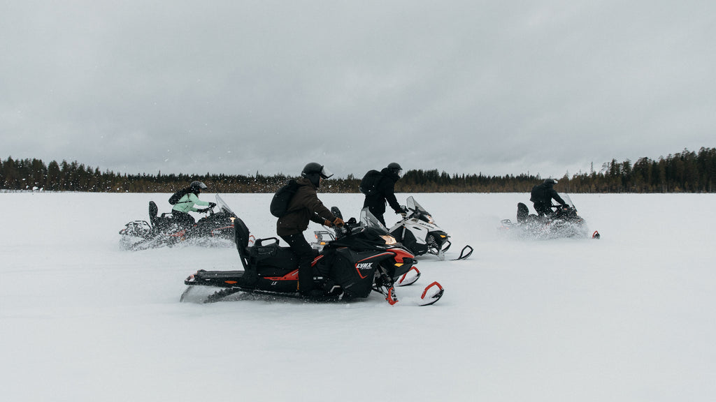 A group of people riding snow mobiles across a field in Finalnd