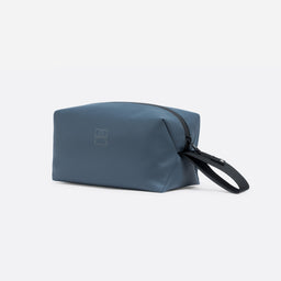 A studio shot of a Tasmin Blue Wash Bag shoeing the front, reflective logo and loop handle