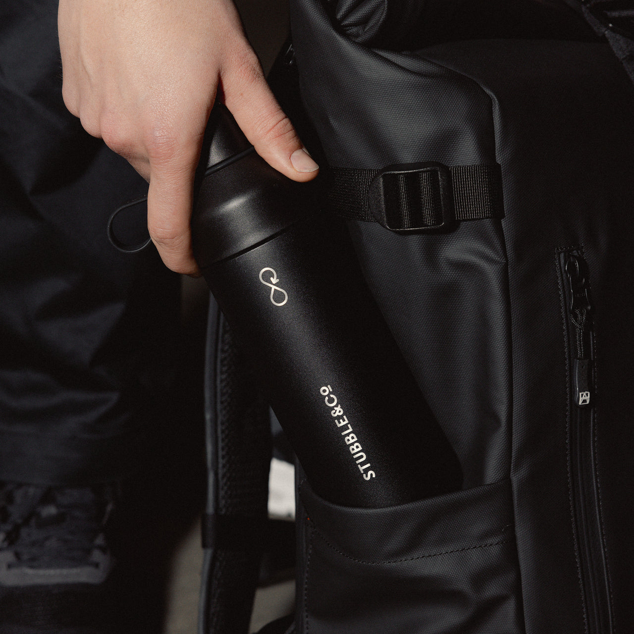A man putting the Black Stubble&Co x Ocean Culture water bottle into the side pocket of a Roll Top 20L